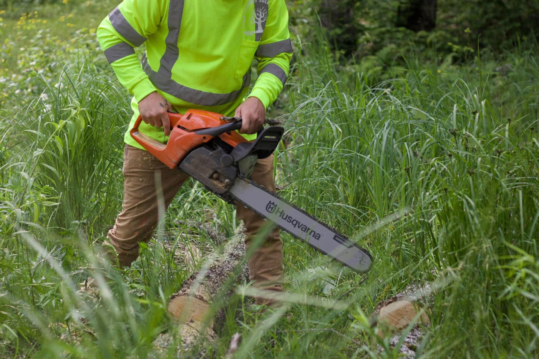 Limb Splitters crew member cutting a downed log with a chainsaw